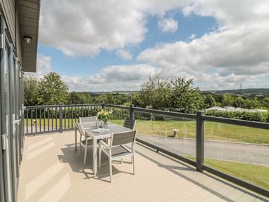 A balcony with a table and four chairs overlooking a grassy area and trees at Ash Lodge in Teigngrace near Newton Abbot