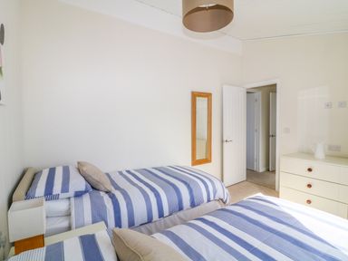 A bedroom with two single beds covered in blue and white striped bedding a white dresser with a jug and a wall mirror at Beech Lodge in Teigngrace near Newton Abbot