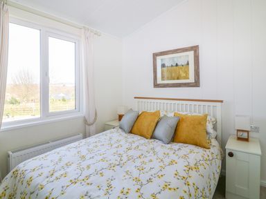 A bedroom with a bed with yellow flower bedding and pillows and a window with curtains at Beech Lodge in Teigngrace near Newton Abbot