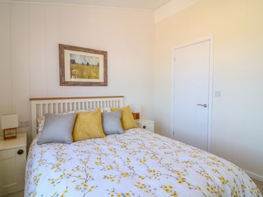 A bedroom with a bed with floral bedspread and pillows bedside tables with lamps and a painting on the wall at Beech Lodge in Teigngrace near Newton Abbot