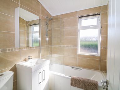 A bathroom with a bathtub shower combination sink cabinet mirror and window at Beech Lodge in Teigngrace near Newton Abbot