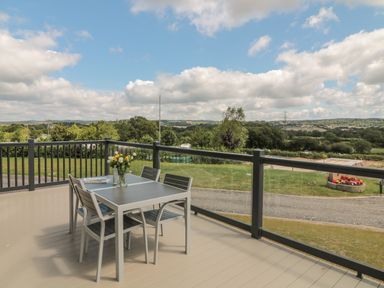 An outdoor deck with a table and four chairs and a vase of flowers overlooking a green landscape at Beech Lodge in Teigngrace near Newton Abbot