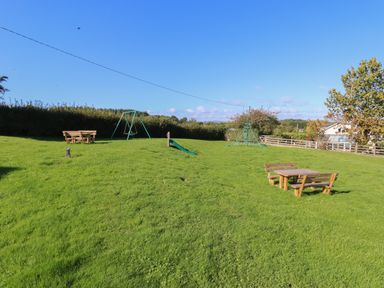 A grassy outdoor area with picnic tables swings and play equipment at Beech Lodge in Teigngrace near Newton Abbot