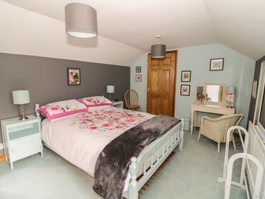 A bedroom with a double bed floral bedding bedside tables lamps a wooden door a writing desk chair and framed pictures on the walls at Cottage on the Common in Westbury-on-Severn