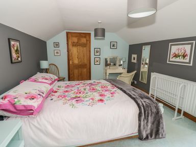 A bedroom with a bed with floral bedding a wooden door a dressing table a chair and framed pictures at Cottage on the Common in Westbury-on-Severn