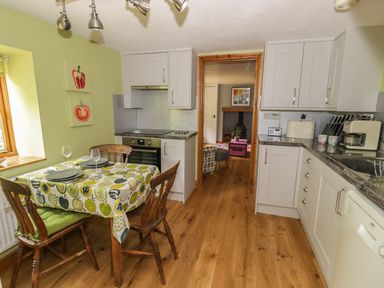 A kitchen with a wooden dining table and chairs next to a window and white cabinets at Cottage on the Common in Westbury-on-Severn