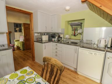 A kitchen with white cabinets appliances and wooden chair at Cottage on the Common in Westbury-on-Severn
