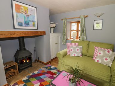 A living room with a green sofa and floral cushions a black wood stove and a colorful rug at Cottage on the Common in Westbury-on-Severn