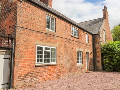 An exterior view of a brick house with multiple windows a door and a gravel ground at Well House Farm Flat 1 in Bretton