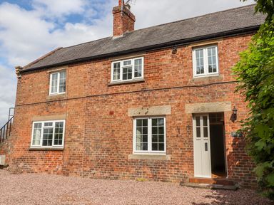 A two-story brick house with white windows and an open white door at Well House Farm Flat 1 in Bretton