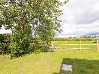 A garden area with two chairs under a tree and a wooden fence with grassy fields beyond at Well House Farm Flat 1 in Bretton