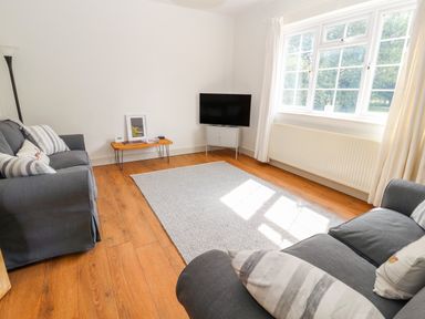 A living room with two gray sofas a small wooden table a television on a stand and a large window at Well House Farm Flat 1 in Bretton