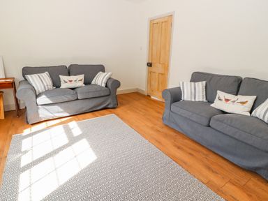 A living room with two gray sofas with cushions a wooden door and a patterned rug on a wooden floor at Well House Farm Flat 1 in Bretton