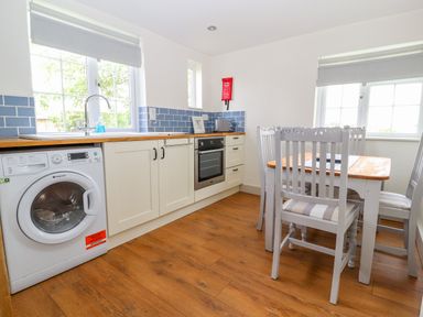 A kitchen with white cabinets blue tiled backsplash wooden table and white chairs at Well House Farm Flat 1 in Bretton