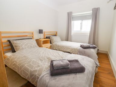 A bedroom with two single beds with grey patterned bedding and towels on each bed with a wooden nightstand and lamp between the beds at Well House Farm Flat 1 in Bretton