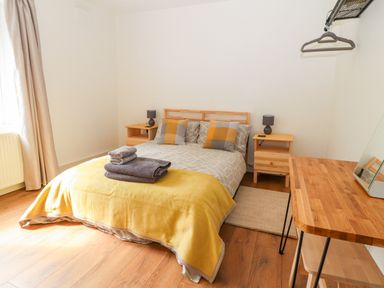 A bedroom with a bed yellow blanket bedside tables and a wooden desk at Well House Farm Flat 1 in Bretton