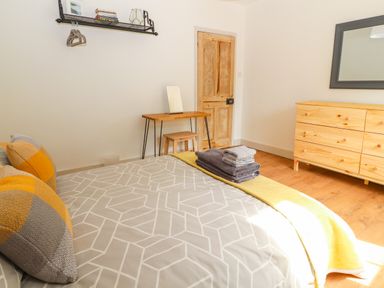 A bedroom with a bed with pillows and folded towels a wooden dresser a mirror a small desk with a stool and a door at Well House Farm Flat 1 Bretton