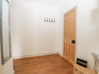 A hallway with wooden flooring a wooden door a wall mirror hooks on the wall and a small wooden shelf with a decorative item at Well House Farm Flat 1 in Bretton