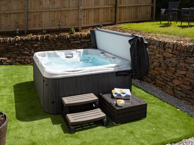 A hot tub with steps and a small table with drinks and snacks in a fenced garden at Be Our Guest Cottage in Chacewater near Truro