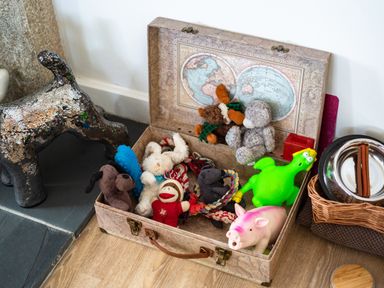 A suitcase filled with various dog toys near a metallic dog statue and a pet feeding area at Be Our Guest Cottage in Chacewater near Truro