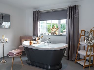 A bathroom with a freestanding bathtub near a window with curtains and decorative items at Be Our Guest Cottage in Chacewater near Truro