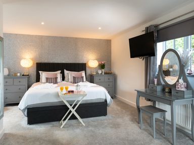 A bedroom with a double bed bedside tables a dressing table and a wall mounted television at Be Our Guest Cottage in Chacewater near Truro
