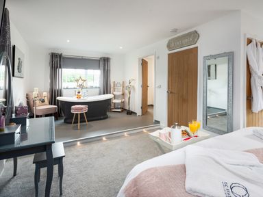 A bedroom with a bed and breakfast tray beside a freestanding bathtub and dressing table at Be Our Guest Cottage in Chacewater near Truro