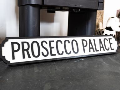 A sign with the words Prosecco Palace on the floor near a black furniture leg and a dog figurine at Be Our Guest Cottage in Chacewater near Truro