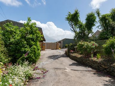 A driveway with plants and flowers on both sides leading to wooden gates at Be Our Guest Cottage in Chacewater near Truro
