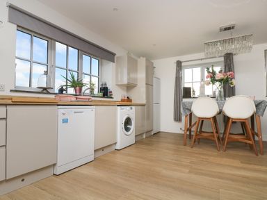 A kitchen with wooden countertops dishwasher washing machine dining table with flowers in a vase and two chairs at Be Our Guest Cottage in Chacewater near Truro