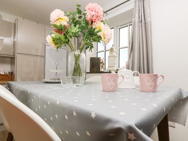 A kitchen table with a star patterned tablecloth flowers in a vase cups and a white teapot at Be Our Guest Cottage in Chacewater near Truro