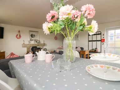 A dining table with a vase of flowers cups a teapot and plates in a living room at Be Our Guest Cottage in Chacewater near Truro