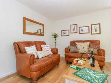 A living room with two brown leather couches a wooden coffee table with a Scrabble game and a cheese plate at Duck Cottage in Sutton Poyntz