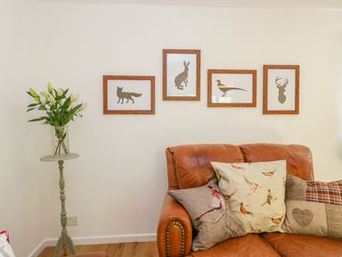 A brown leather sofa with four decorative pillows and four framed animal silhouettes on a white wall at Duck Cottage in Sutton Poyntz