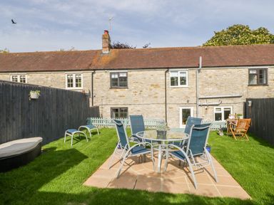 A garden with a glass table and blue chairs on a paved area at Duck Cottage in Sutton Poyntz