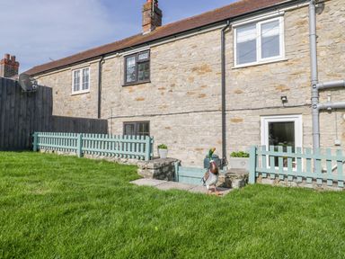 A stone house with a small garden and green grass with a decorative duck sculpture at Duck Cottage in Sutton Poyntz
