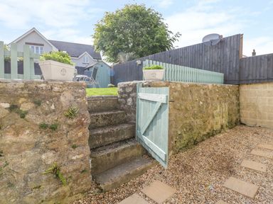Garden with stone steps leading to grass area with chairs and shed at Duck Cottage in Sutton Poyntz