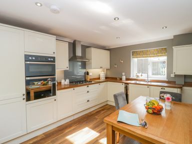 A kitchen with white cabinets a wooden table and a fruit bowl at Duck Cottage in Sutton Poyntz