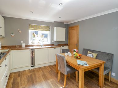A kitchen with wooden floors a wooden dining table with chairs and a bench near a window with yellow patterned blinds at Duck Cottage in Sutton Poyntz