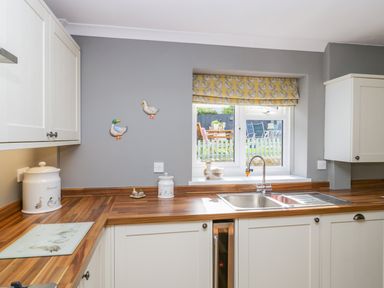 A kitchen with wooden countertops white cabinets a window with a yellow patterned blind and decorative ducks on the wall at Duck Cottage in Sutton Poyntz