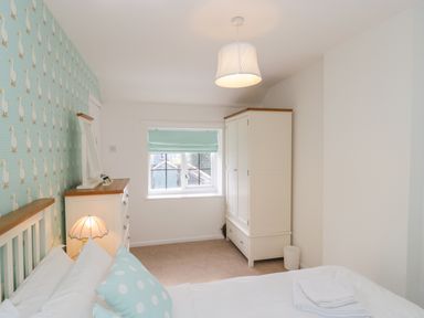 A bedroom with a bed pillow wallpaper wardrobe and chest of drawers at Duck Cottage in Sutton Poyntz