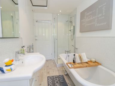 A bathroom with a bathtub, shower, sink, rubber duck, and bath tray at Duck Cottage in Sutton Poyntz
