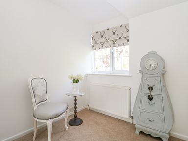 A small room with a chair a round side table with flowers a window and a clock cabinet at Duck Cottage in Sutton Poyntz