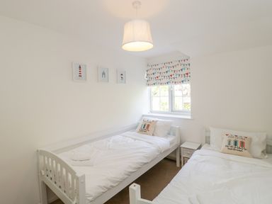 A bedroom with two single beds a window with patterned blinds and framed pictures on the wall at Duck Cottage in Sutton Poyntz