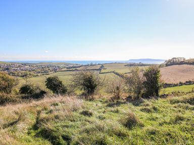 A rural landscape with grassy fields bushes and a distant village near the coast at Duck Cottage in Sutton Poyntz