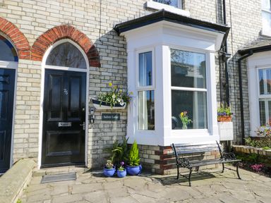The front entrance of a brick house with a black door and a bay window with flowers in pots and a bench outside at Sailors Lodge in Filey