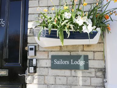 A wall with a planter of flowers above a sign reading Sailors Lodge beside a black door at Sailors Lodge in Filey