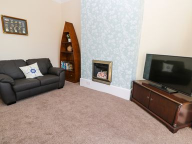 A living room with a leather sofa a wooden boat-shaped shelf a wall-mounted fireplace and a television on a wooden cabinet at Sailors Lodge in Filey