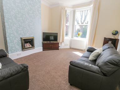 A living room with two black sofas a fireplace and a TV on a stand at Sailors Lodge in Filey