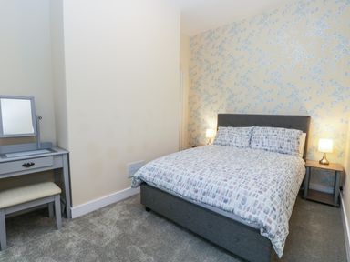 A bedroom with a double bed two bedside tables with lamps a dressing table with stool and patterned wallpaper at Sailors Lodge in Filey